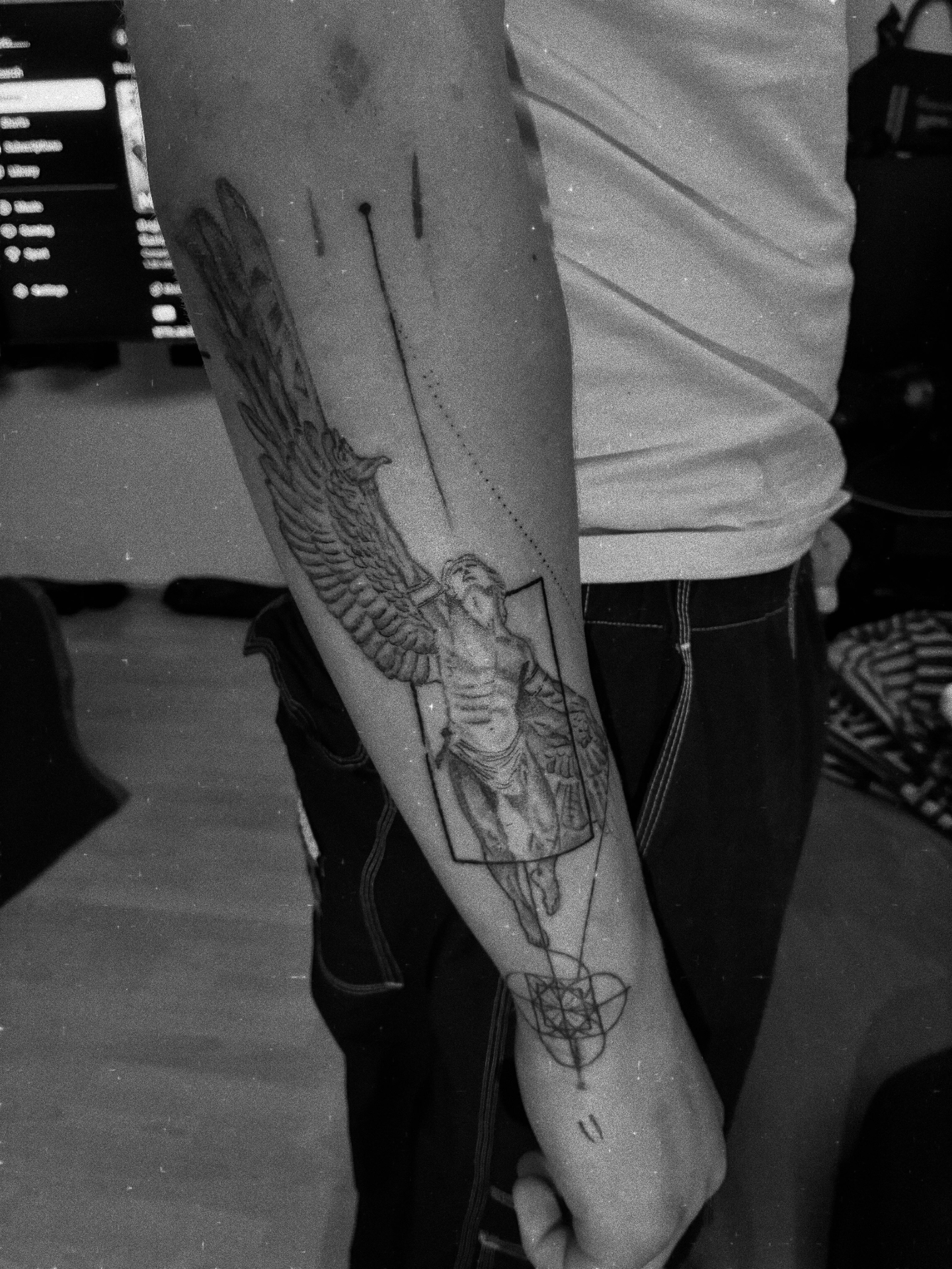 Black and grey realism tattoo of a winged angel statue with geometric linework on a forearm