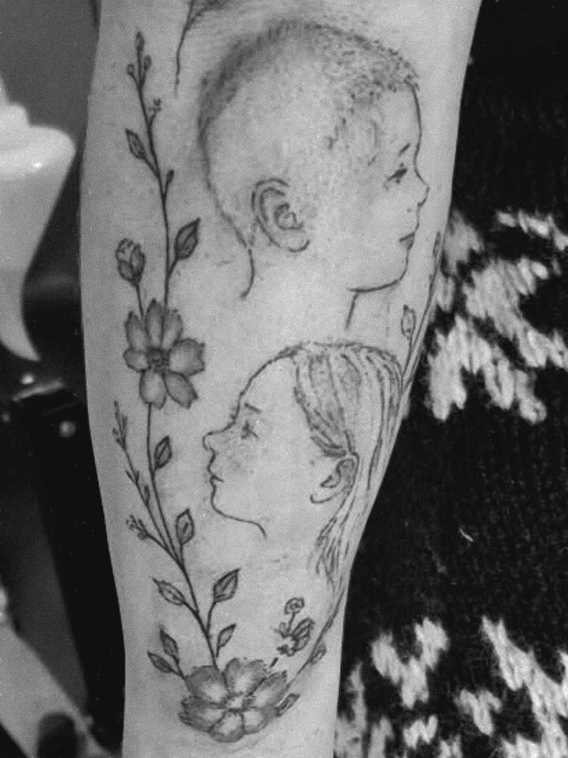 Fine line portrait tattoo of two children with floral detail on a lower leg
